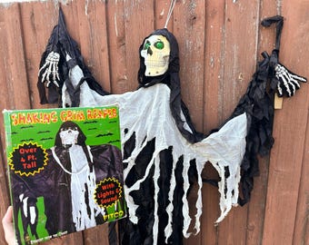 May include: A Halloween decoration of a Shaking Grim Reaper with a skull head, black cloak, and white tattered fabric. The box reads "Shaking Grim Reaper Over 4 Ft. Tall With Lights & Sound".