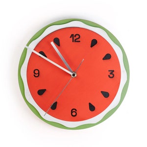 Könnte beinhalten: Eine rote und grüne Wassermelonen-Uhr mit schwarzen Zahlen und Zeigern. Das Zifferblatt der Uhr hat einen weißen Rand und schwarze Kerne.
