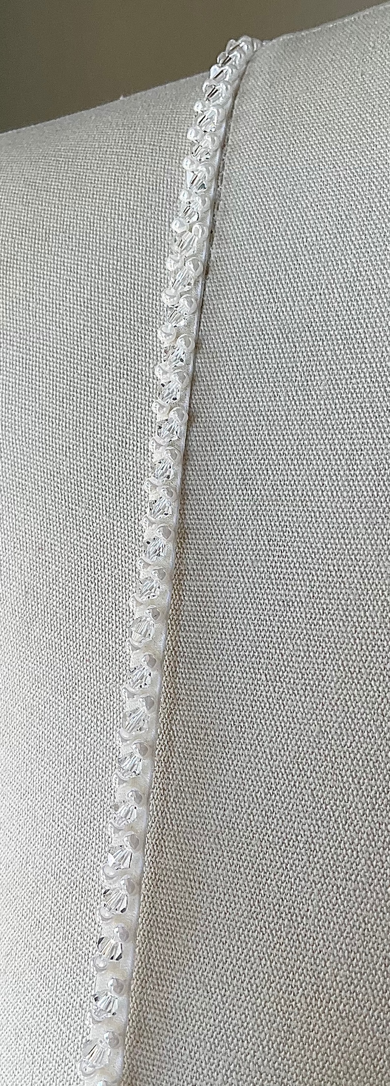May include: A close-up of a white beaded trim. The trim is made of small, round beads that are sewn together in a continuous line. The beads are arranged in a staggered pattern, creating a subtle texture.