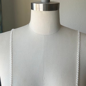 May include: White beaded straps for a dress or top. The straps are made of small, white beads that are strung together on a clear thread.