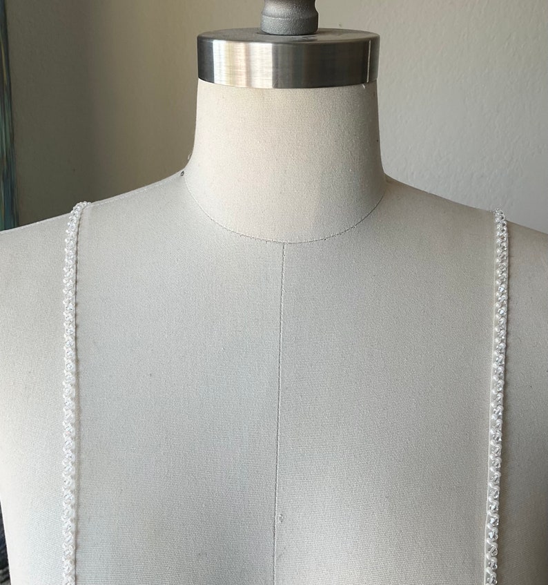 May include: White beaded straps for a dress or top. The straps are made of small, white beads that are strung together on a clear thread.