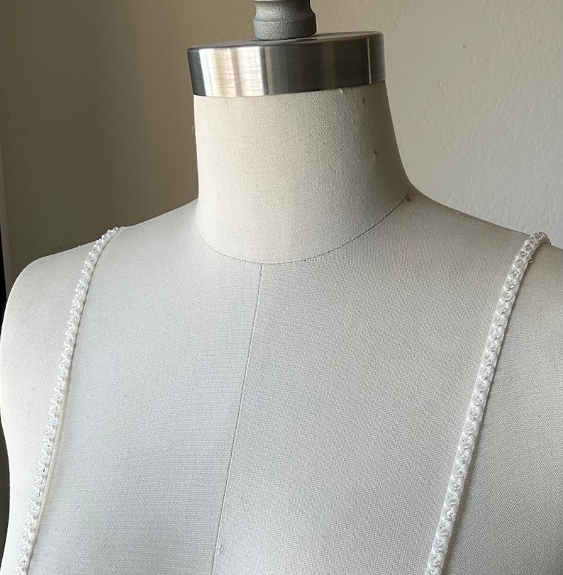 May include: White beaded straps for a dress or top. The straps are made of small, white beads that are sewn together.