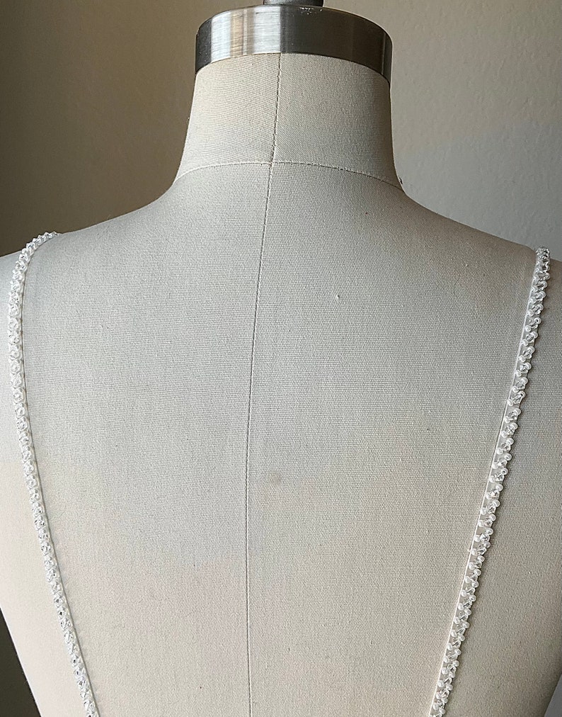 May include: White beaded straps for a wedding dress or other formal attire. The straps are made of small, white beads that are sewn together to create a delicate and elegant look.