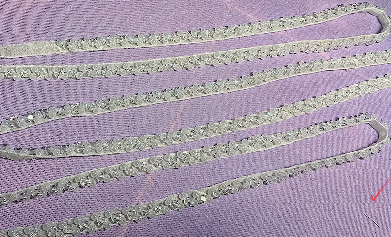 May include: White beaded trim with a sheer backing. The trim is arranged in four rows on a purple surface.