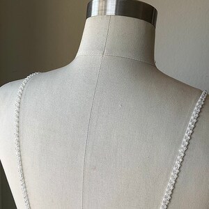 May include: A white dress with beaded straps on a white dress form.