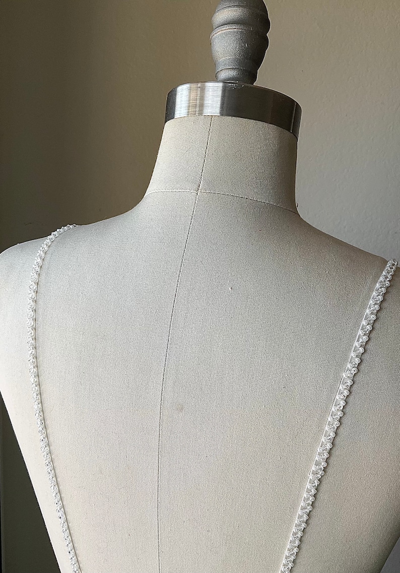 May include: A white dress with beaded straps on a white dress form.
