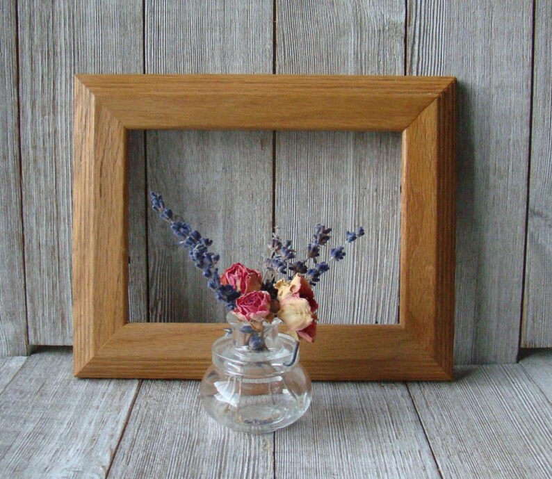 May include: A wooden picture frame with a simple design, featuring a small glass vase with dried flowers inside. The flowers are a mix of lavender and pink roses.