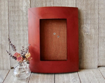May include: A red wooden picture frame with a slightly rounded top and bottom. The frame is empty and ready to hold a photo or artwork.