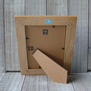 May include: The back of a wooden picture frame with a cardboard easel. The frame is a light brown color and has a simple design.