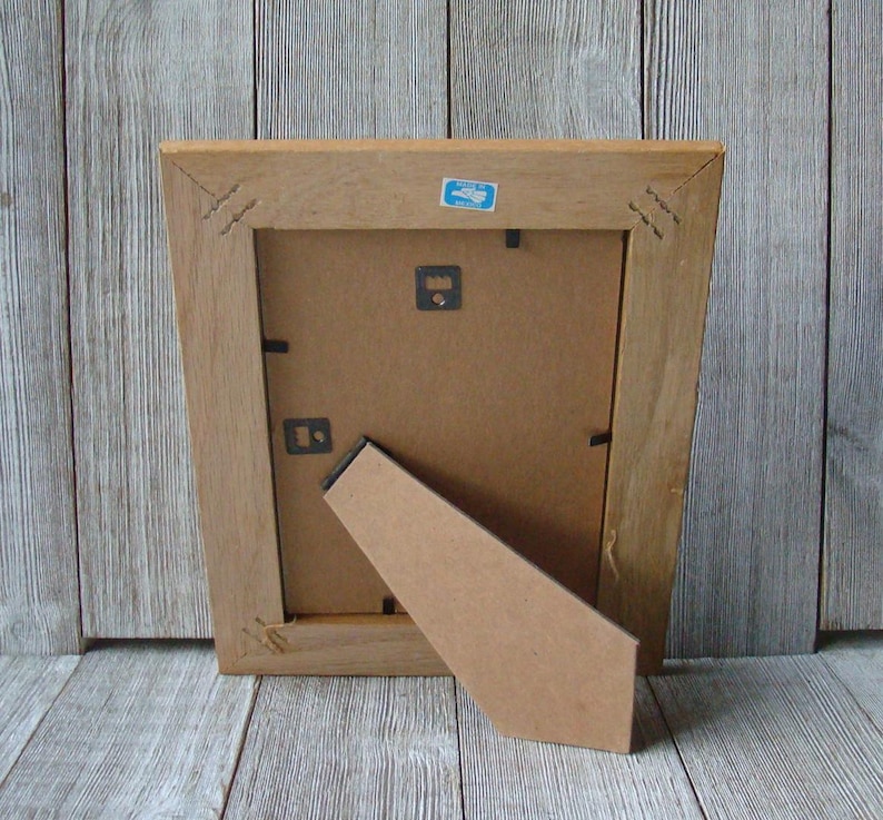 May include: The back of a wooden picture frame with a cardboard easel. The frame is a light brown color and has a simple design.