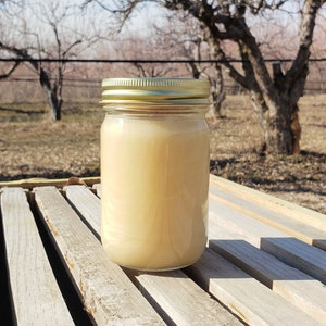 May include: A glass jar with a gold lid filled with a light brown liquid. The jar is sitting on a wooden surface.