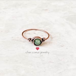May include: A delicate copper wire ring featuring a green gemstone. The ring is simple and elegant, ideal for everyday wear.
