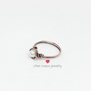 May include: A simple copper wire ring with a white pearl accent. The ring is handmade and features a delicate design.