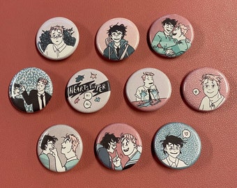 May include: Ten round, colorful pins featuring characters from the graphic novel "Heartstopper". The pins are all different colors and feature different characters from the book. The pins are all about 1 inch in diameter.