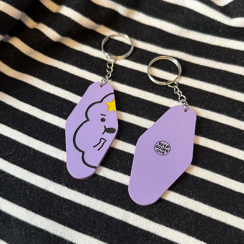 May include: Two purple keychains with a cartoon character and the text "Keep Going Club" on the back.