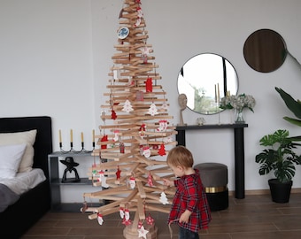 May include: A wooden Christmas tree decorated with red and white ornaments. A young child is standing next to the tree, reaching for an ornament.