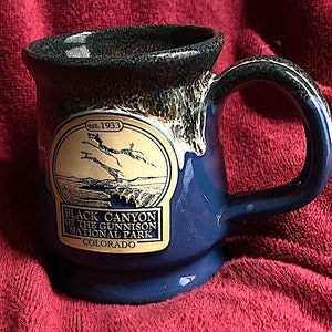 May include: Blue ceramic mug with a brown glaze and a gold logo that reads "Black Canyon of the Gunnison National Park, Colorado, est. 1933".