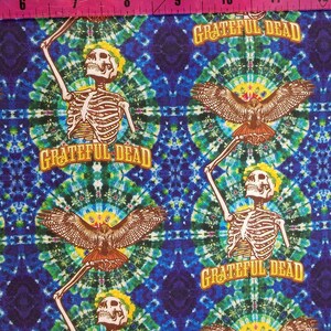 Pode incluir: Um tecido colorido com um padrão repetitivo de esqueletos, falcões e as palavras "Grateful Dead". O fundo é um padrão tie-dye em tons de azul, verde e amarelo.