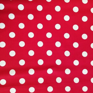 May include: A close-up of a red fabric with a pattern of evenly spaced white polka dots. The dots are circular and appear to be the same size. The fabric is slightly wrinkled.