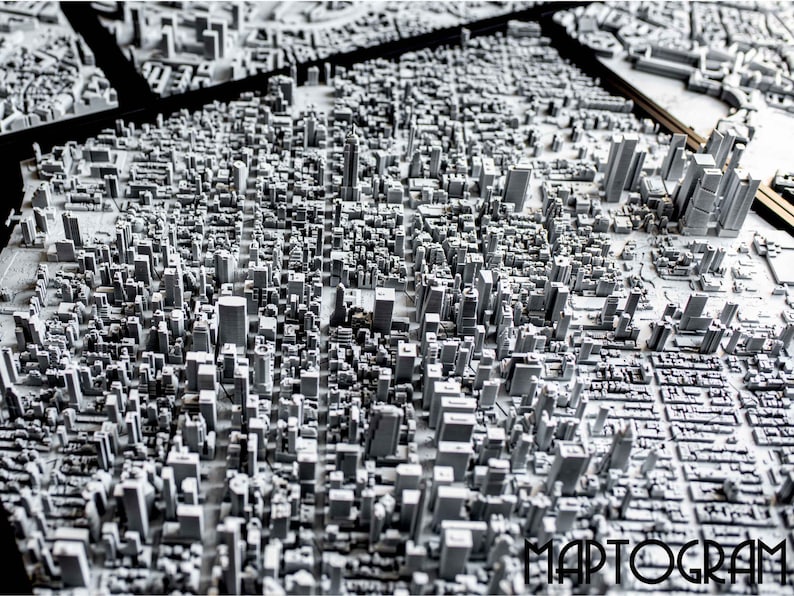 May include: A detailed 3D model of a city skyline, with buildings rendered in shades of gray. The model is set on a black surface and features the word "MAPTOGRAM" in the lower right corner.