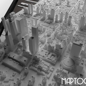 May include: A 3D model of a city skyline with tall buildings and a circular structure in the center. The model is made of white plastic and is set against a white background. The word "MAPTOGRAM" is printed in black at the bottom of the image.