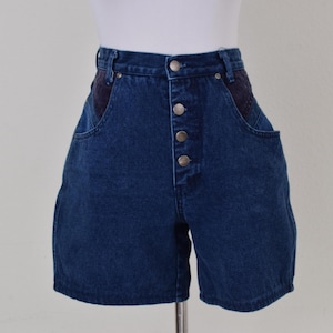 Könnte beinhalten: Dunkelblaue Jeansshorts mit hoher Taille und Knopfverschluss. Die Shorts haben ein klassisches Fünf-Taschen-Design mit dunkelblauen Stoffakzenten auf den Vordertaschen. Die Shorts werden auf einer Schaufensterpuppe präsentiert.