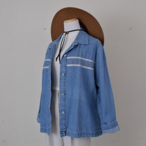 May include: A light blue denim jacket with silver embellishments and white embroidery. The jacket has a button-up front and long sleeves.