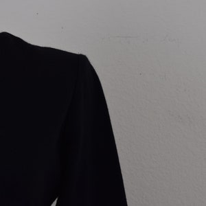 Pu&ograve; includere: Una camicia nera a maniche lunghe con collo alto.