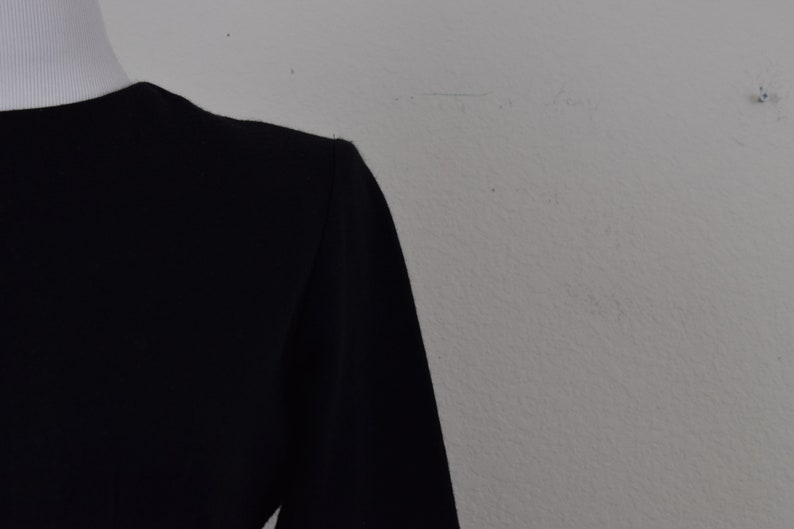 Pu&ograve; includere: Una camicia nera a maniche lunghe con collo alto.