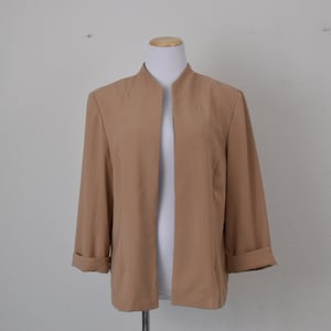 May include: A tan blazer with a mandarin collar and long sleeves. The blazer is open in the front and has a slightly fitted silhouette.