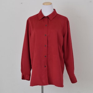 Puede incluir: Una camisa de manga larga con botones de color rojo oscuro. La camisa tiene un cuello clásico y un corte holgado.