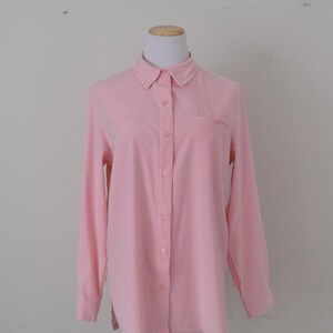 May include: A light pink button-down shirt with long sleeves and a small pocket on the left chest. The shirt is displayed on a mannequin against a plain white background. The shirt has a classic collar and button closures.