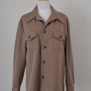 Puede incluir: Una camisa marrón de manga larga con cierre de botones y dos bolsillos grandes en el pecho.