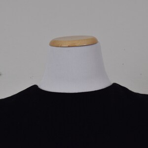 Pu&ograve; includere: Una camicia nera a maniche lunghe con collo rotondo.