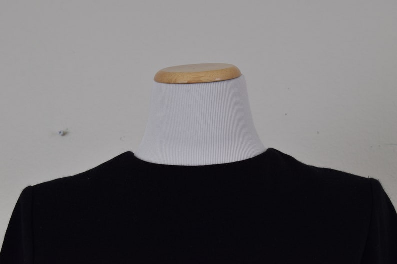 Pu&ograve; includere: Una camicia nera a maniche lunghe con collo rotondo.