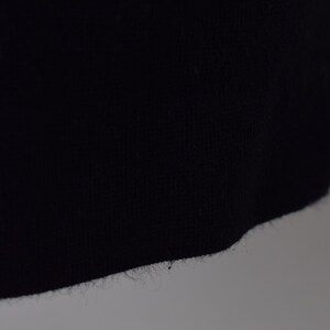 Pu&ograve; includere: Primo piano del bordo inferiore di un capo di abbigliamento blu scuro, che mostra la trama del tessuto e un bordo leggermente sfilacciato.