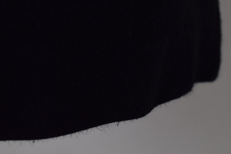 Pu&ograve; includere: Primo piano del bordo inferiore di un capo di abbigliamento blu scuro, che mostra la trama del tessuto e un bordo leggermente sfilacciato.