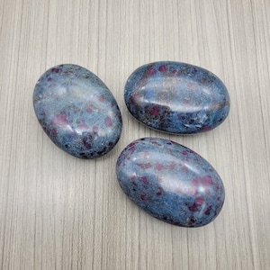 May include: Three smooth, oval-shaped stones with a blue-grey base and irregular patches of deep red. The stones are polished, suggesting they are gemstones. They could be used for decoration or for their metaphysical properties.