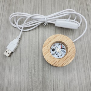 May include: A white USB cable with a switch and a round wooden base with a circuit board and LED lights. The base is connected to the cable and has a USB connector on the other end.