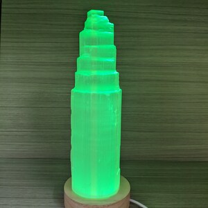 May include: A green Himalayan salt lamp with a wooden base. The lamp is lit and emits a warm glow.