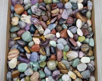 Puede incluir: Una caja blanca llena de piedras pulidas de varios colores, incluyendo verde, marrón, rojo, morado y azul.