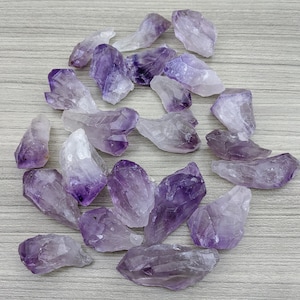 Peut inclure: Une collection de pointes de cristal d'améthyste de différentes tailles et nuances de violet. Les cristaux sont disposés sur une surface en bois gris clair.