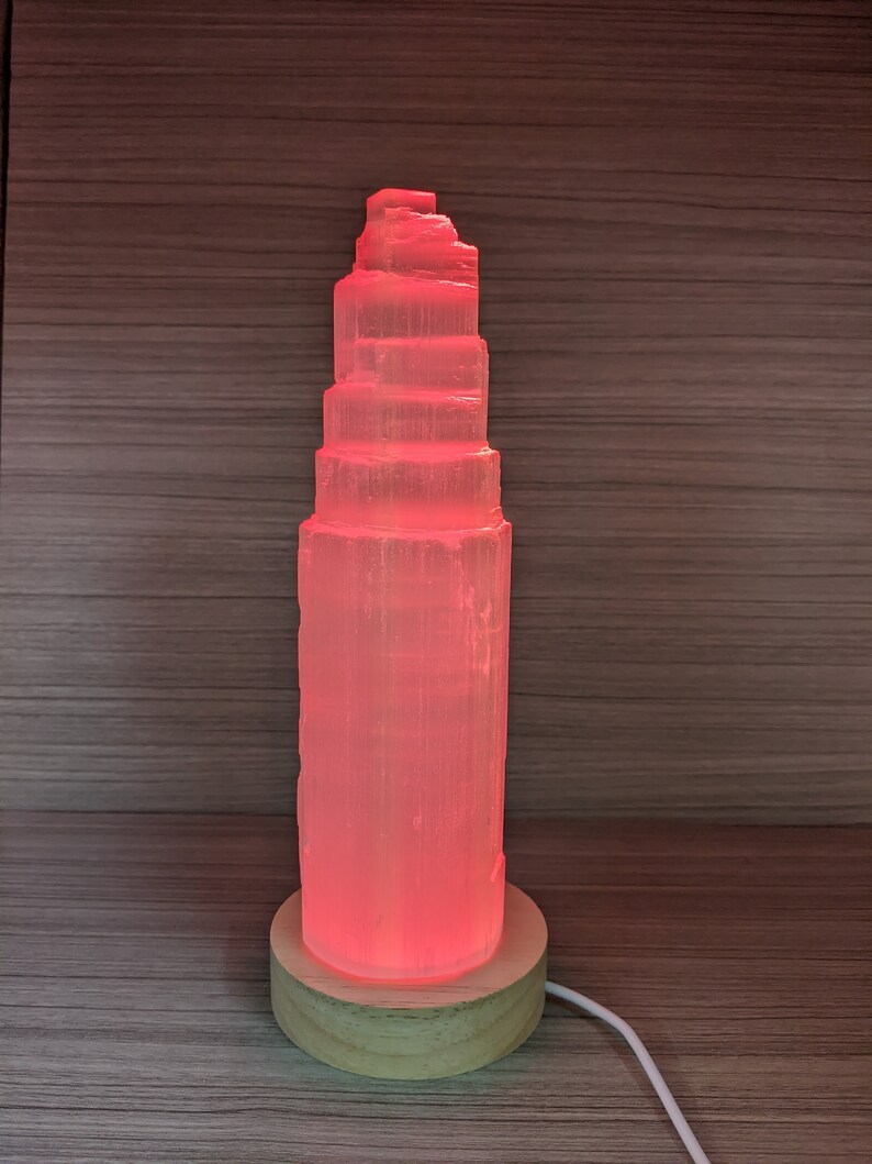 May include: A pink Himalayan salt lamp with a wooden base. The lamp is lit and glowing a warm pink colour.