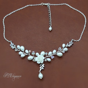 May include: A delicate silver necklace with a white pearl and crystal floral design. The necklace features a single white rose and a dangling pearl.