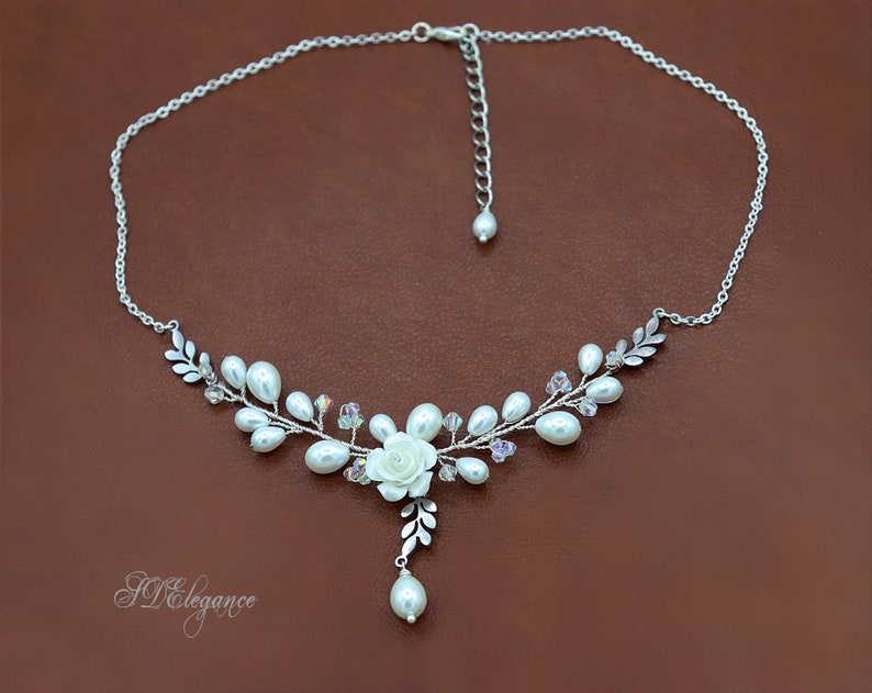 May include: A delicate silver necklace with a white pearl and crystal floral design. The necklace features a single white rose and a dangling pearl.