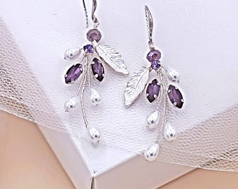 Könnte beinhalten: Ein Paar silberfarbene Ohrhänger mit violetten, marquise-geschliffenen Kristallen, weißen tropfenförmigen Kunstperlen und silberfarbenen Metallblättern. Die Ohrringe hängen an silberfarbenen Haken und sind oben mit kleinen violetten Perlen verziert.