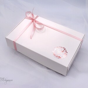 May include: A white gift box with a pink ribbon tied in a bow. The box has a sticker with the word "Thank You" in a gold foil wreath.