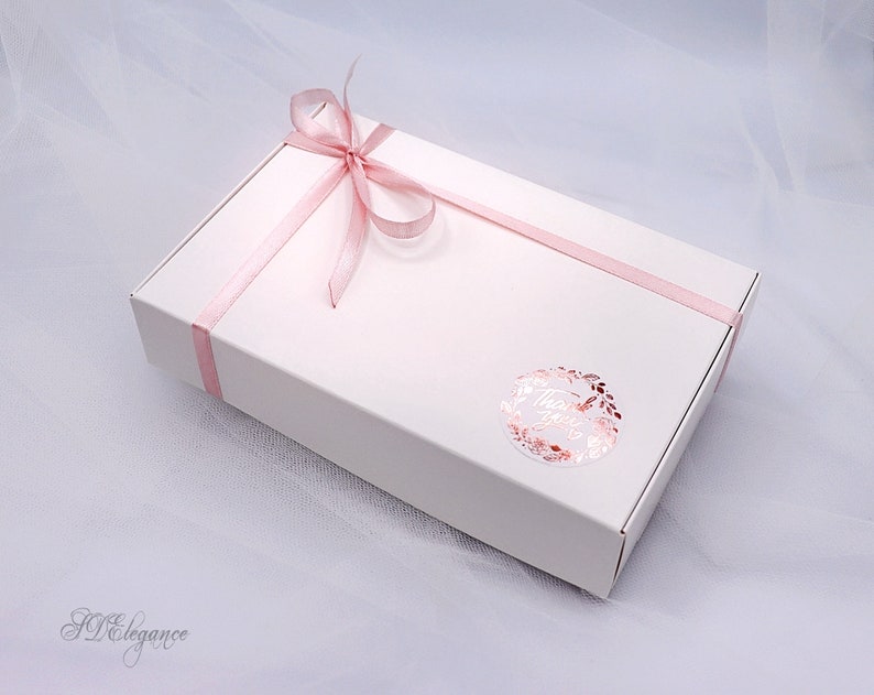 May include: A white gift box with a pink ribbon tied in a bow. The box has a sticker with the word "Thank You" in a gold foil wreath.