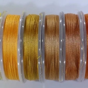 May include: Ten spools of thread in various shades of yellow, orange, and brown. The thread is wound around clear plastic spools.