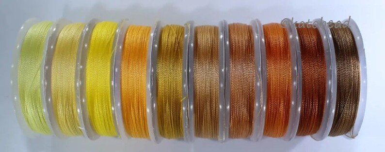 May include: Ten spools of thread in various shades of yellow, orange, and brown. The thread is wound around clear plastic spools.